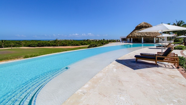 A poolside area with lounge chairs and a thatched-roof structure. - Golden Bear Getaway (Punta Cana)