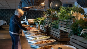 A buffet setup with various food dishes and a person serving. - Hotell Hallstaberget (Solleftea)