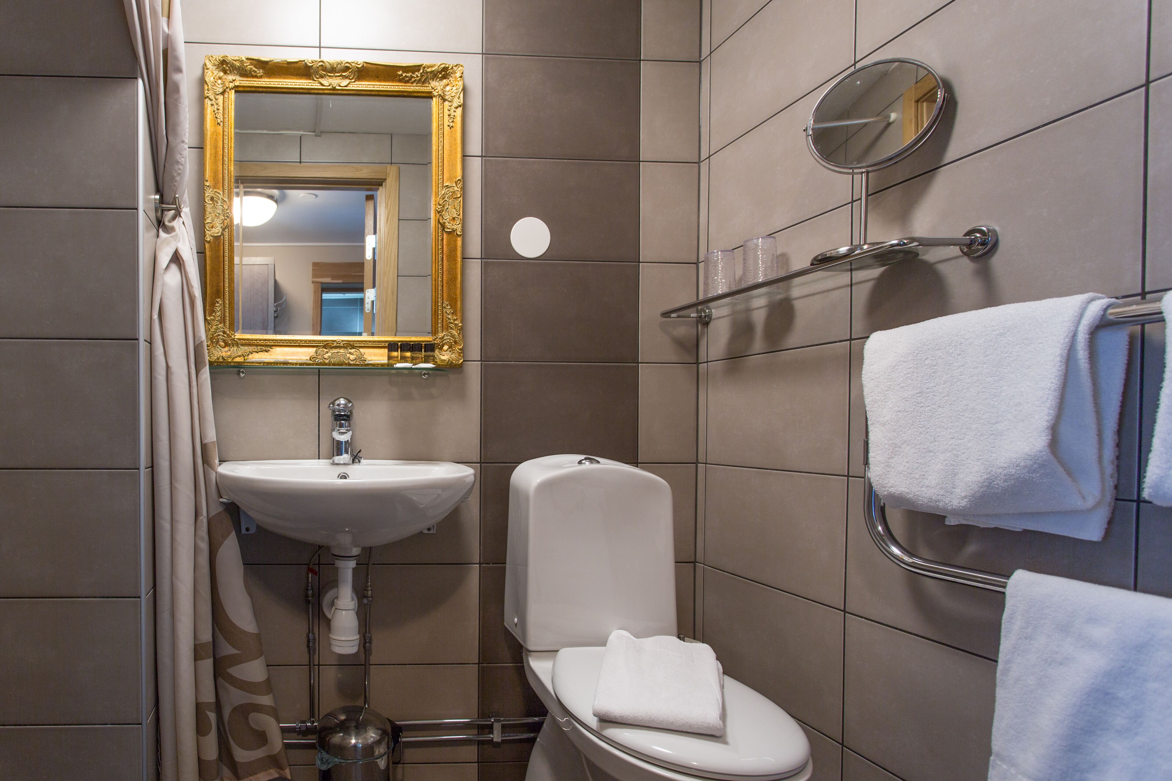 Een badkamer met een wit wastafel, toilet, spiegel met gouden lijst en een handdoekrek met opgevouwen handdoeken.