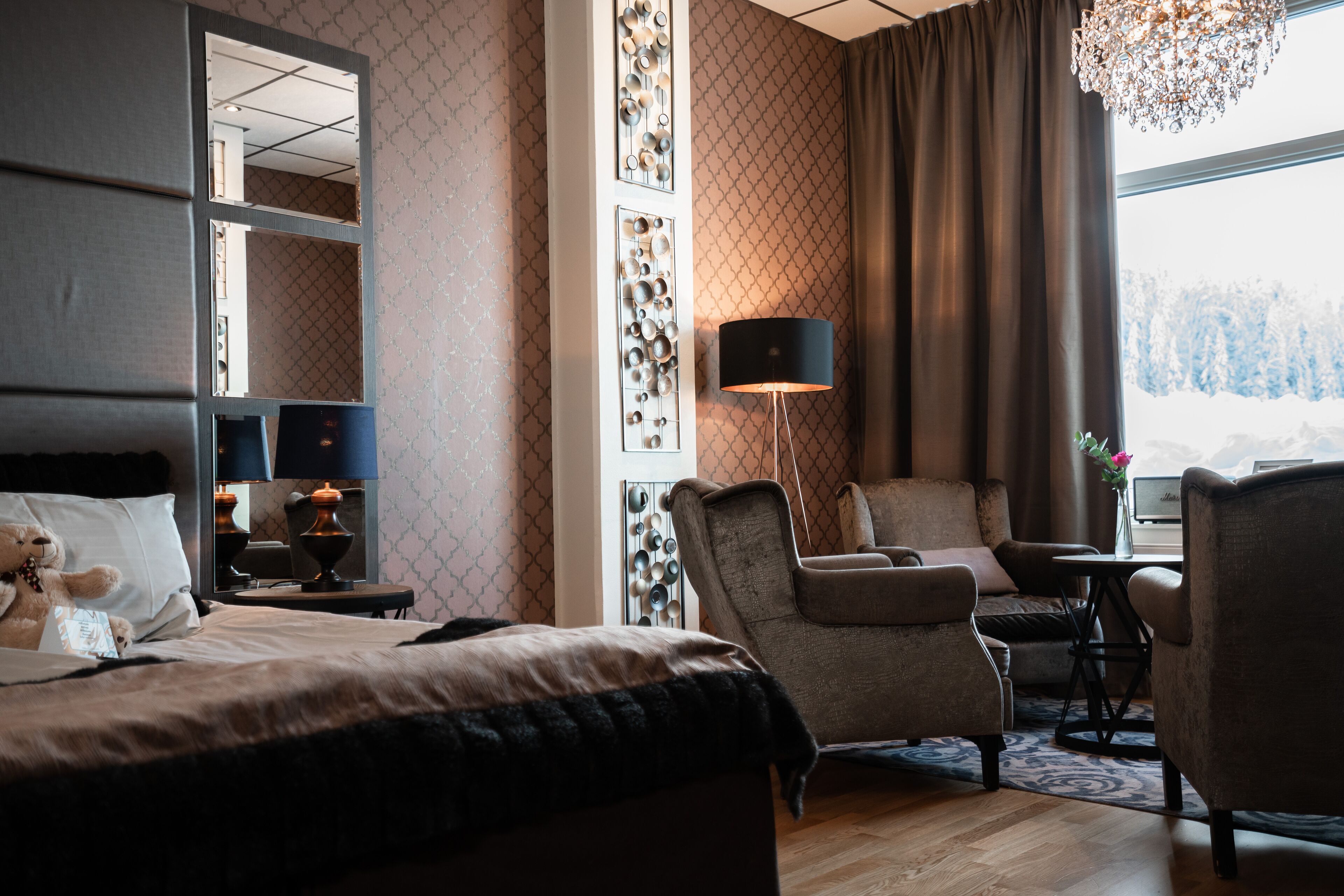 A hotel room with a bed, a sofa, a chair, a lamp, and a large window with a view of trees.