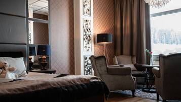 A hotel room with a bed, a sofa, a chair, a lamp, and a large window with a view of trees.