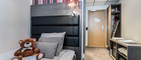 Una habitación de hotel moderna con una cama, un peluche, una lámpara y un armario.