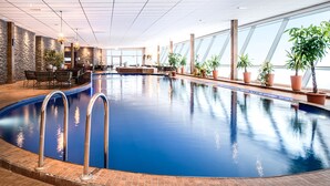 An indoor swimming pool with clear blue water, surrounded by potted plants and a seating area with chairs and tables. - Hotell Hallstaberget (Solleftea)