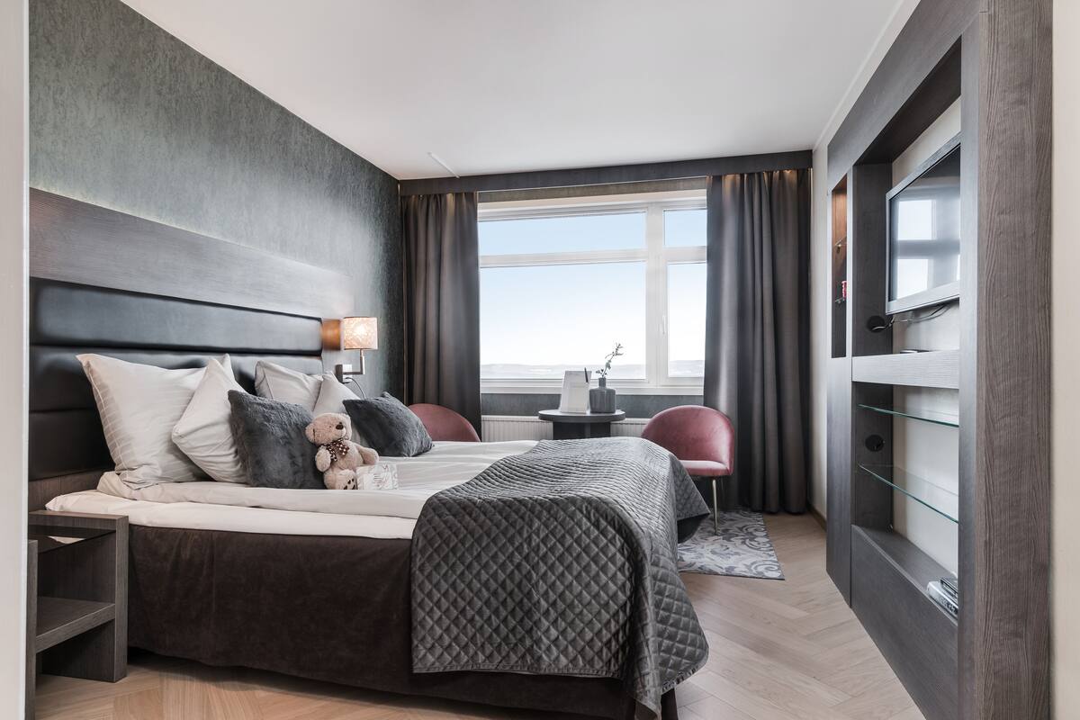 Ein modernes Hotelzimmer mit einem großen Bett, einem Schreibtisch, einem Stuhl, einem Fernseher und Blick auf die Stadt.