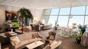A spacious lounge area with multiple seating options, a large potted plant, and a view of the sky through large windows. - Hotell Hallstaberget (Solleftea)