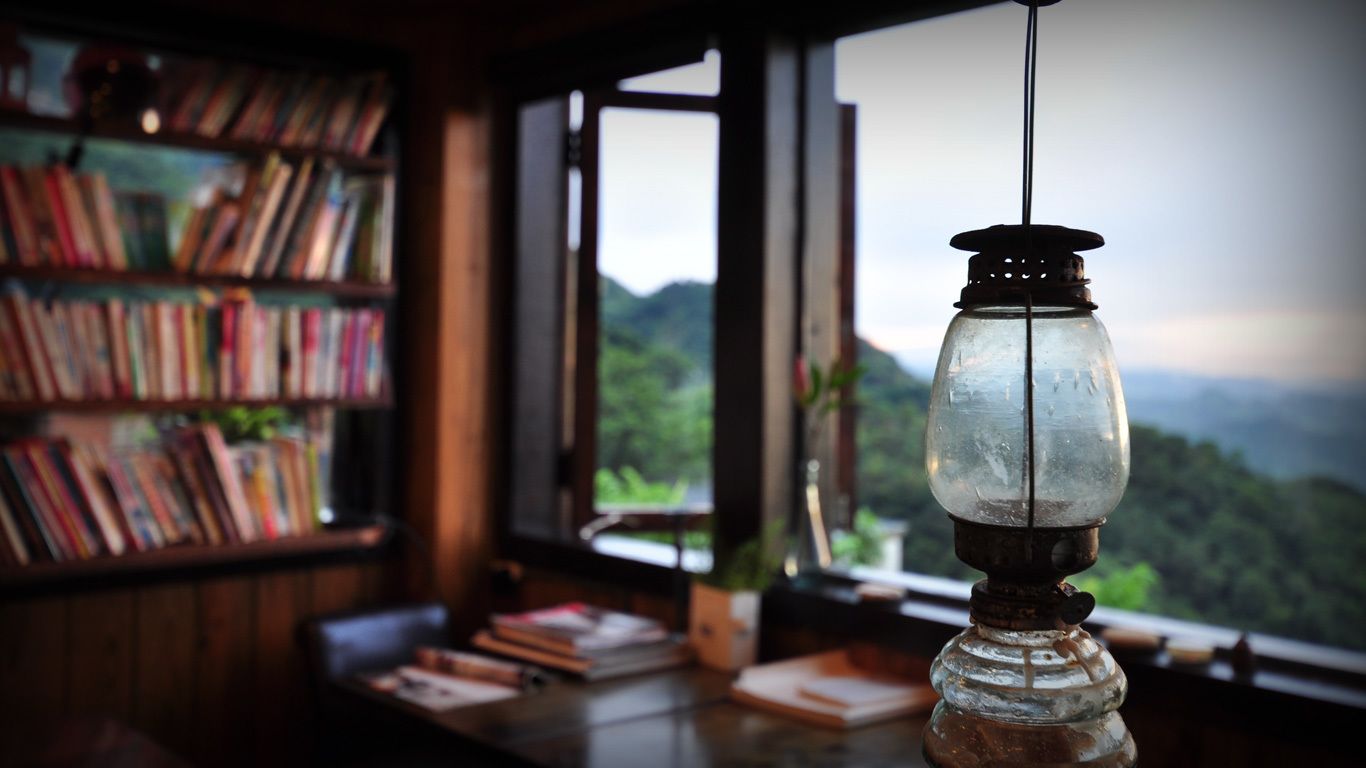 A room with a bookshelf, a table with books, and a view of a mountainous landscape through a window.
