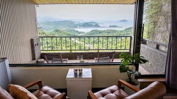 Un balcón con vistas a colinas verdes y una masa de agua. Hay dos sillones de cuero y una mesita con una taza y un platillo.
