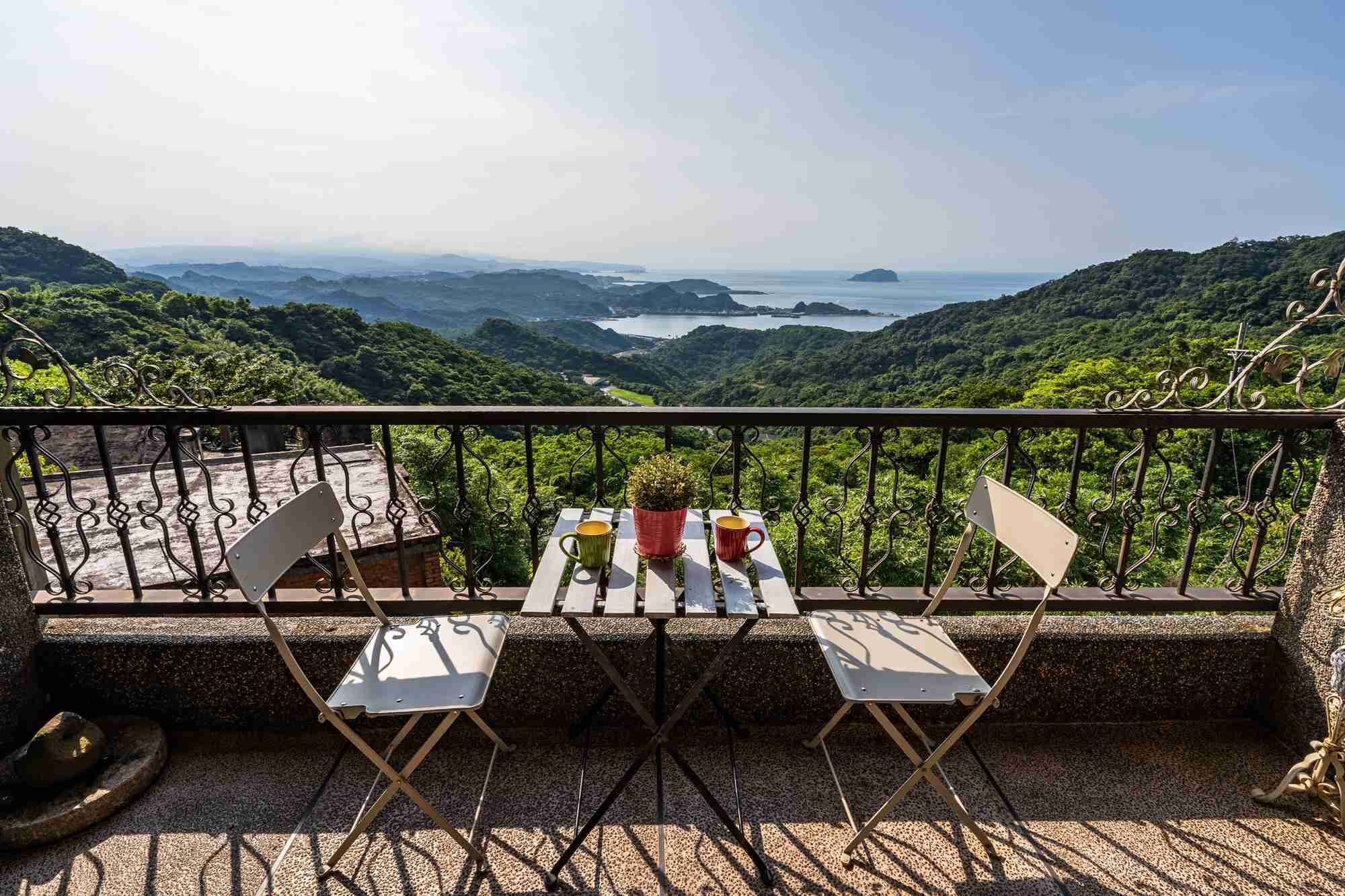 A balcony with a table and chairs overlooking a mountainous landscape.