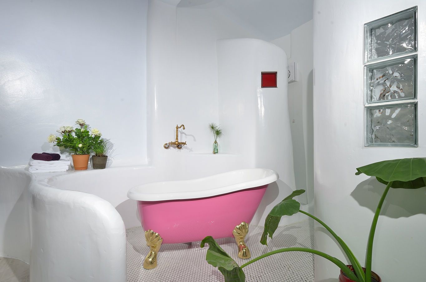 Une salle de bain avec une baignoire blanche, une baignoire rose et un lavabo blanc. On y trouve des serviettes, une plante en pot et un petit vase sur le comptoir.