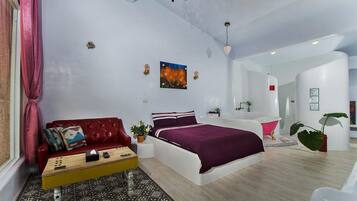 Un dormitorio moderno con cama, un sofá rojo, una mesita y un baño con bañera.