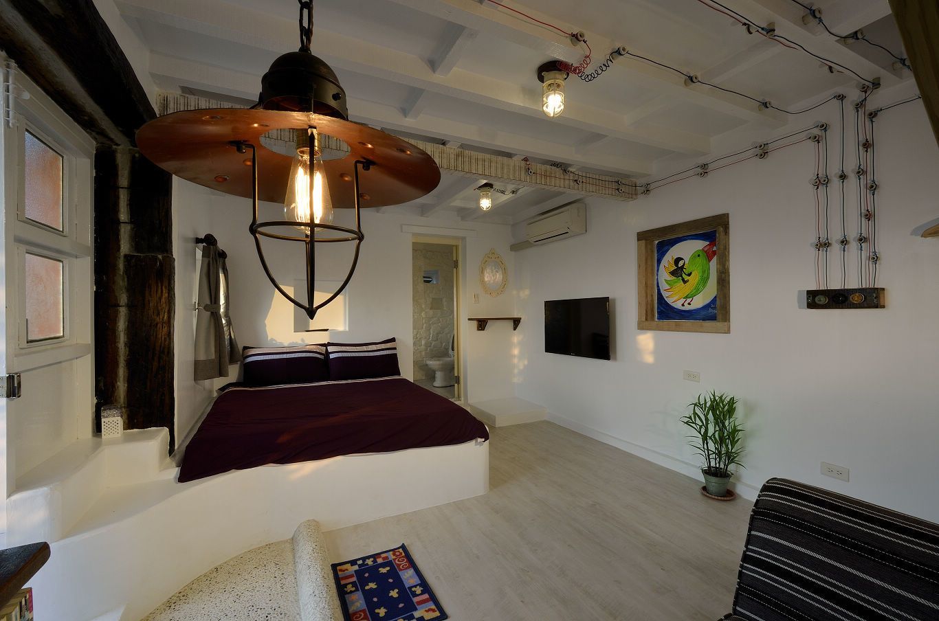 Un dormitorio moderno con una cama grande, una lámpara colgante, un televisor y un cuadro en la pared.