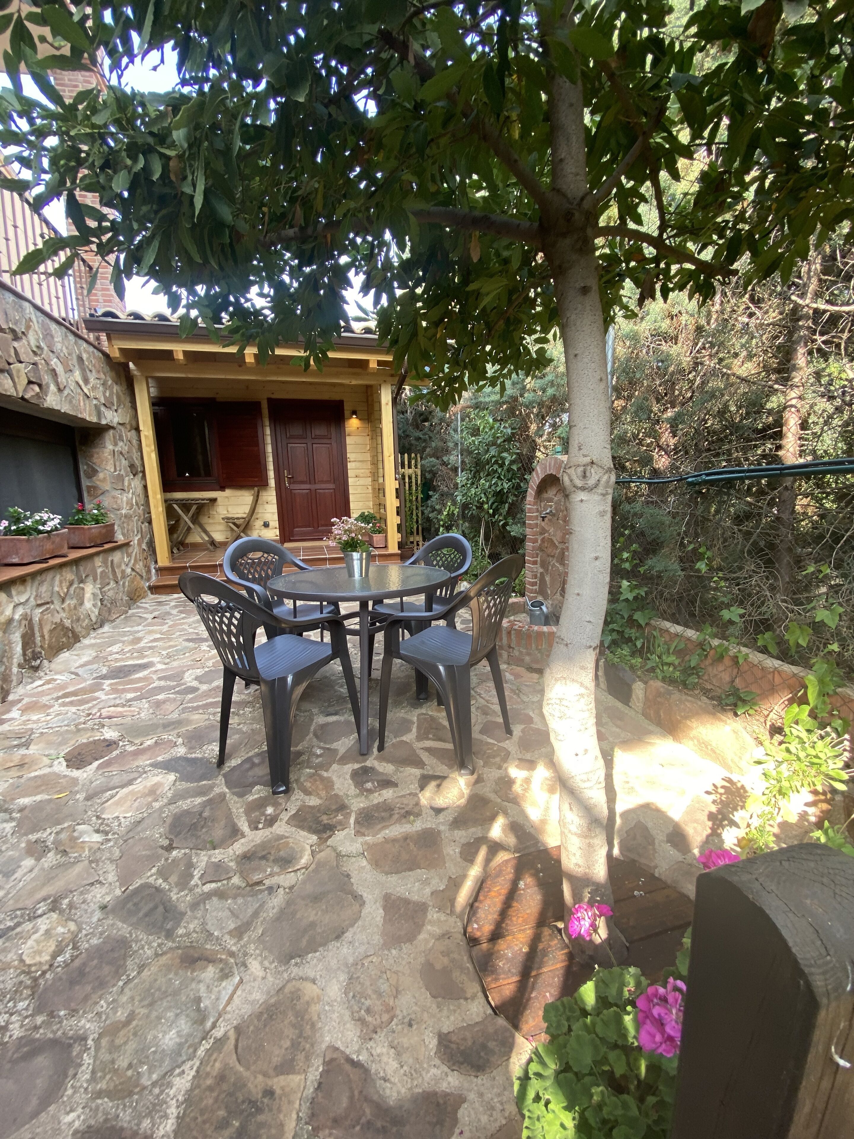 Un patio de piedra con una mesa redonda y sillas, una puerta de madera y un muro de piedra.