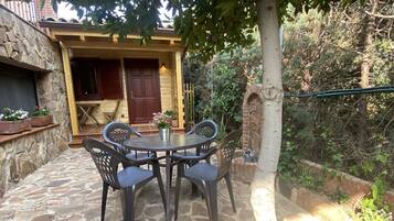 Un patio de piedra con una mesa redonda y sillas, una puerta de madera y un muro de piedra.