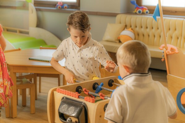 A child playing with a toy table saw in a room with a sofa and a window. - Family Hotel Posta (Santa Cristina Val Gardena)