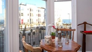 A balcony with a wooden table, chairs, and a view of buildings. - Marina by the Sea B&B (Brighton)