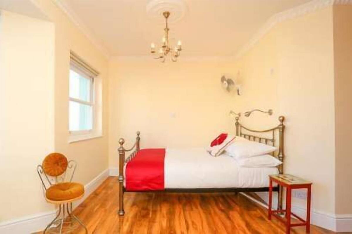 Une chambre avec un plancher en bois, un lit recouvert d’une couvre-lit rouge et blanc, une chaise, une petite table et un lustre.