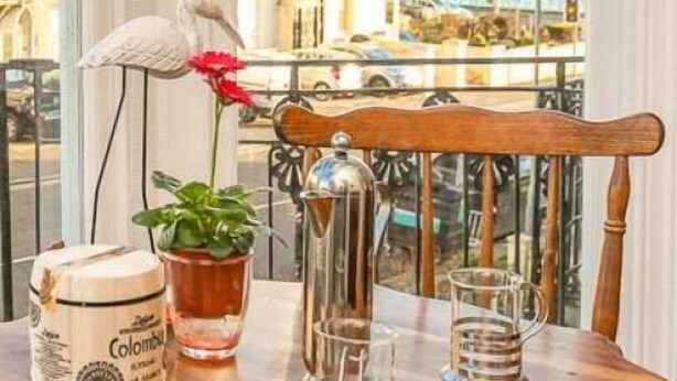 A table with a potted plant, a glass jar, and a metal pitcher on a balcony with a view of buildings and the sea. - Marina by the Sea B&B (Brighton)