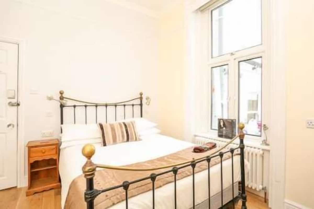 Une chambre à coucher avec un lit, une table de chevet, une fenêtre et un radiateur.