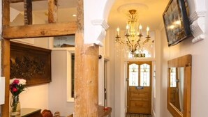 A hallway with a wooden column, a chandelier, a wooden door with stained glass, and a mirror on the wall. - Marina by the Sea B&B (Brighton)