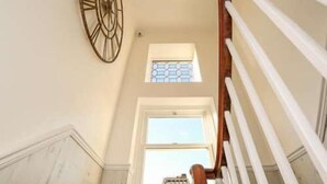 A staircase with a wooden handrail, a clock on the wall, and a window with a toy car on the windowsill. - Marina by the Sea B&B (Brighton)