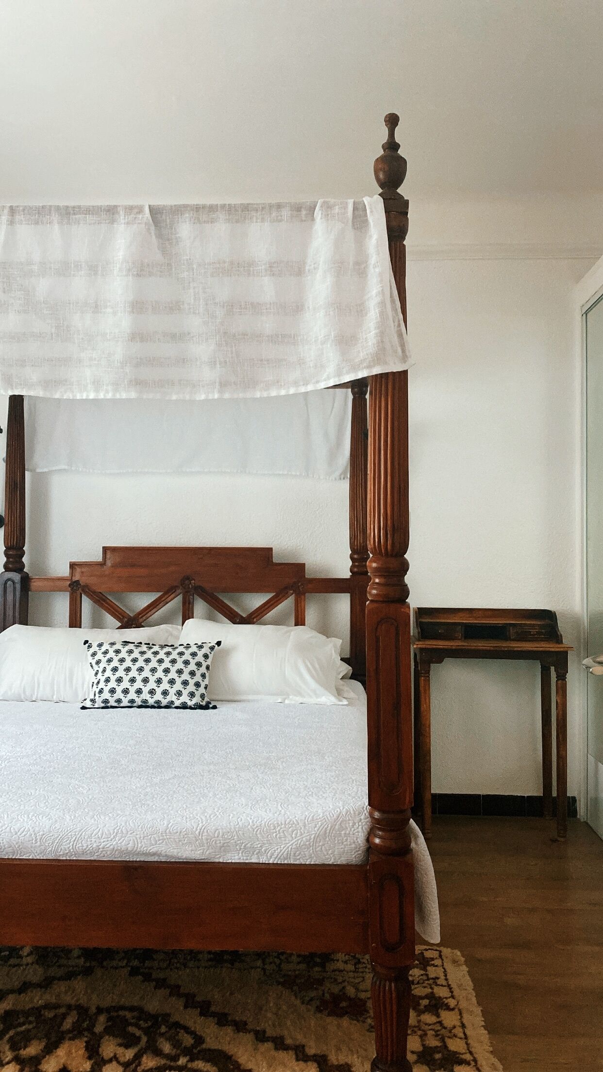 A four-poster bed with a canopy, a wooden headboard, and a patterned pillow.
