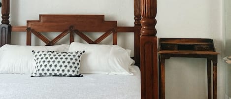 Una cama con dosel, cabecera de madera y almohada estampada.