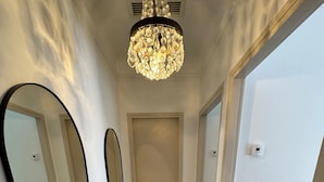 Un pasillo con suelo de madera, un candelabro y dos puertas.