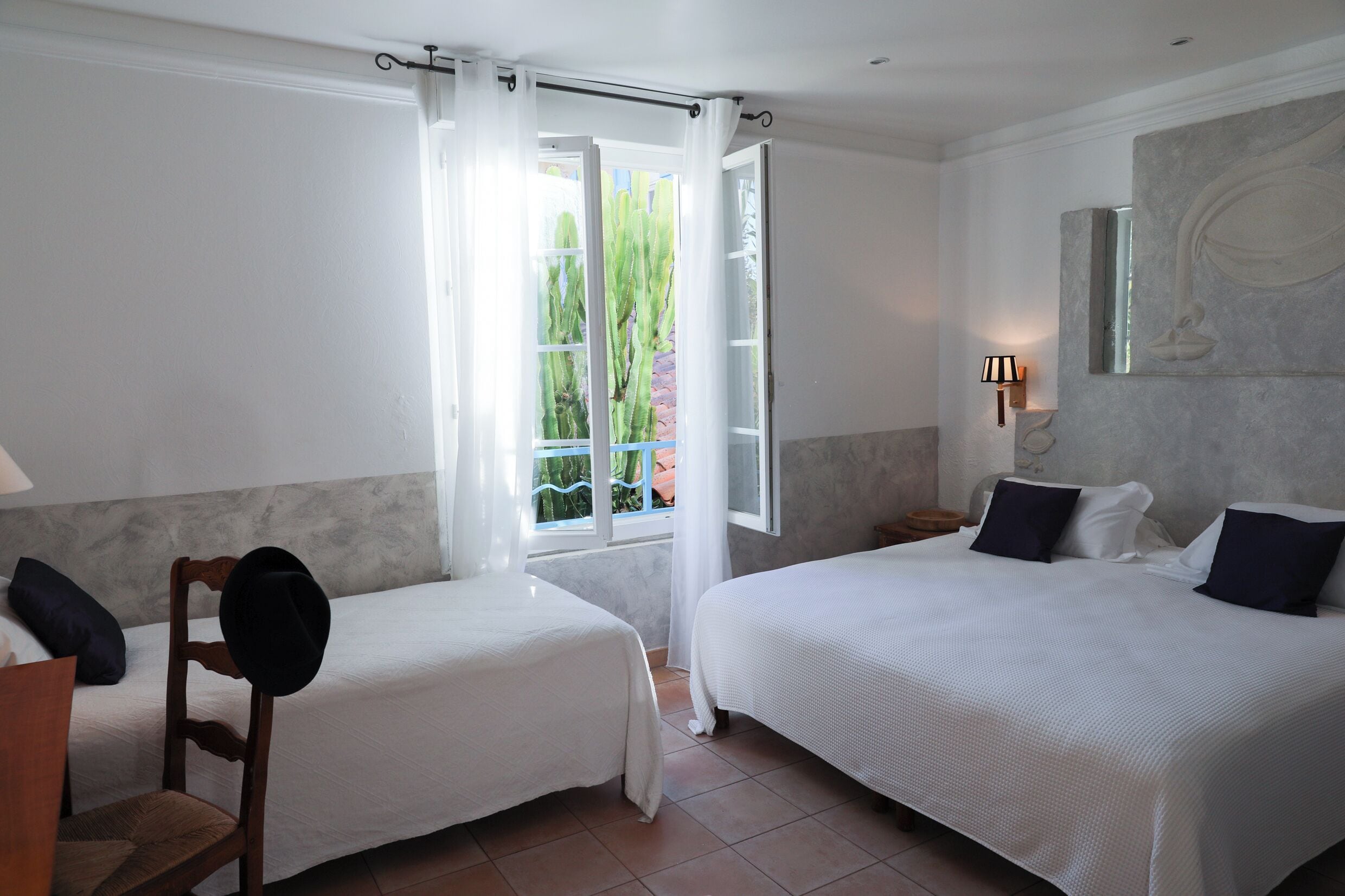 Une chambre d’hôtel avec deux lits, une fenêtre avec des rideaux, une lampe et une œuvre d’art accrochée au mur.