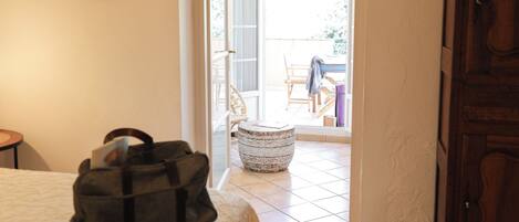 A hotel room with a bed, a suitcase, a hat, a wooden cabinet, and a view of the outdoor patio through an open door.