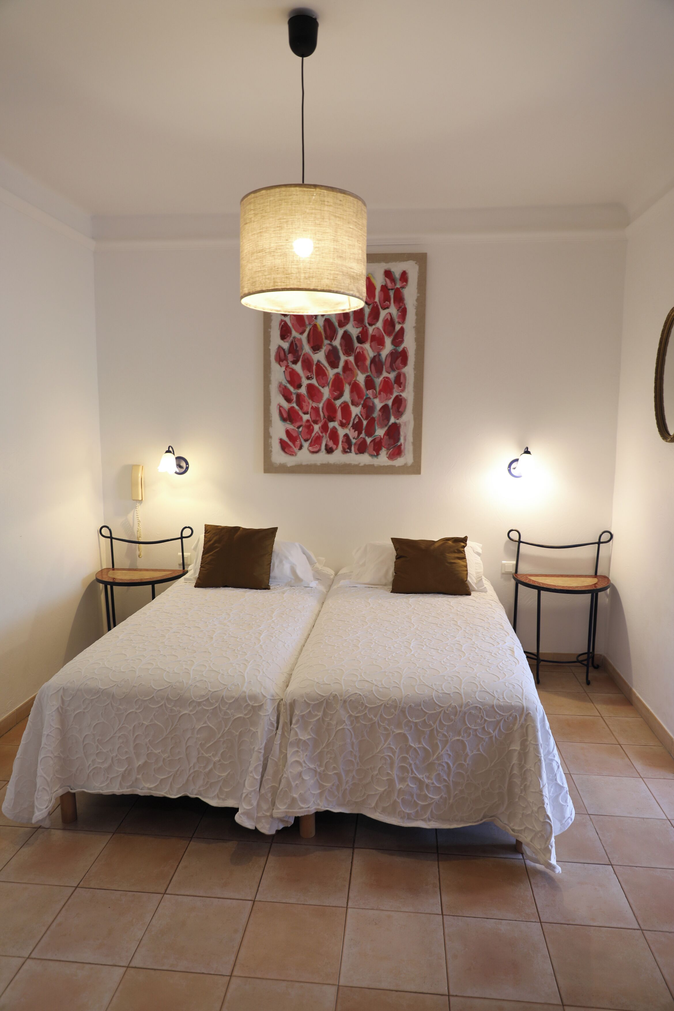 Een tweepersoonsbed met witte lakens, twee nachtkastjes met lampen, een kunstwerk aan de muur en een hanglamp.