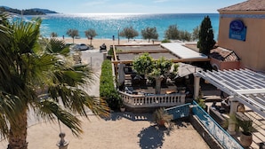 Un hotel con terraza y vistas a una playa, palmeras y el mar.