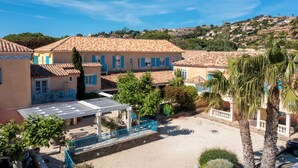 Un edificio de estilo mediterráneo con tejados de teja, una zona de estar al aire libre cubierta y vistas a una colina con otros edificios.