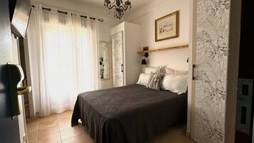 Une chambre à coucher avec un lit, une table de chevet, un miroir et une fenêtre avec des rideaux.