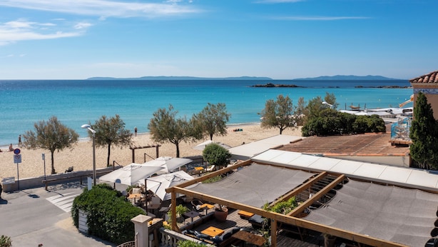 Un patio frente a la playa con mobiliario exterior y sombrillas, con vista a una playa de arena y el mar.