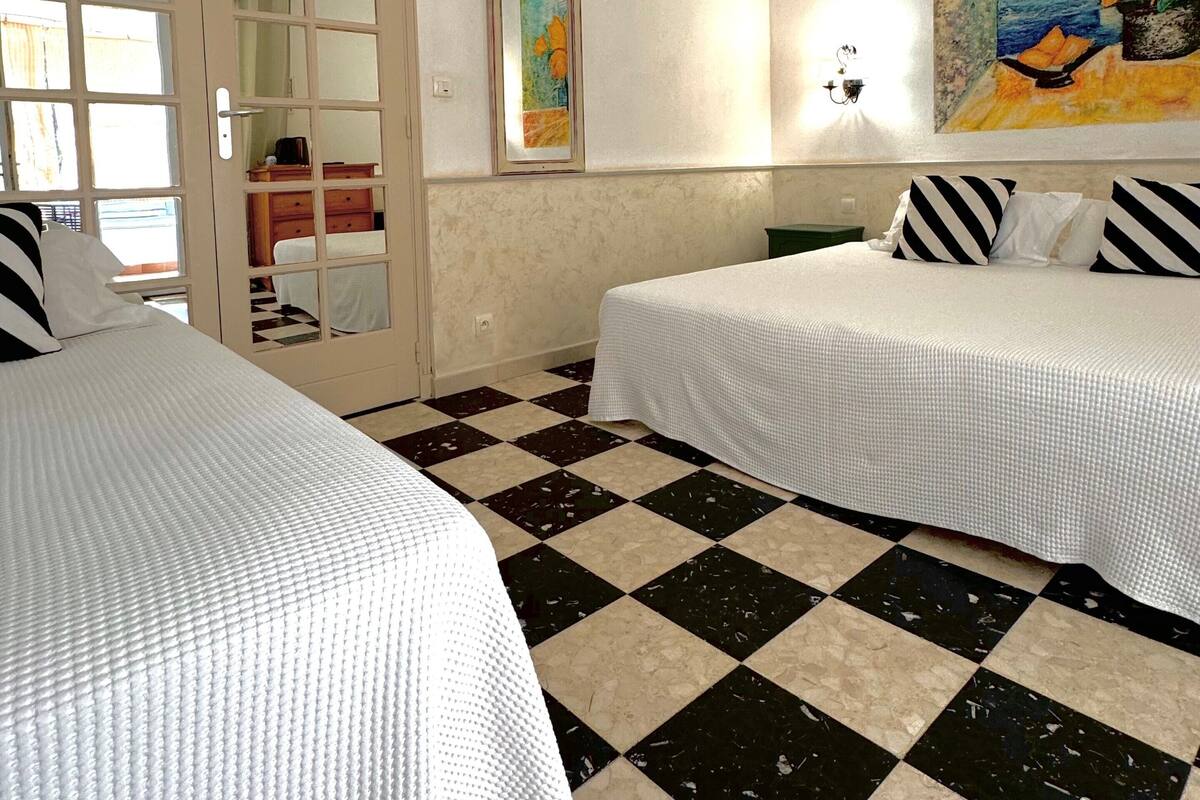 A hotel room with two beds, checkered floor, a painting on the wall, and a mirror.