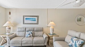 Un salon avec deux canapés, un ventilateur de plafond et un tableau encadré accroché au mur.