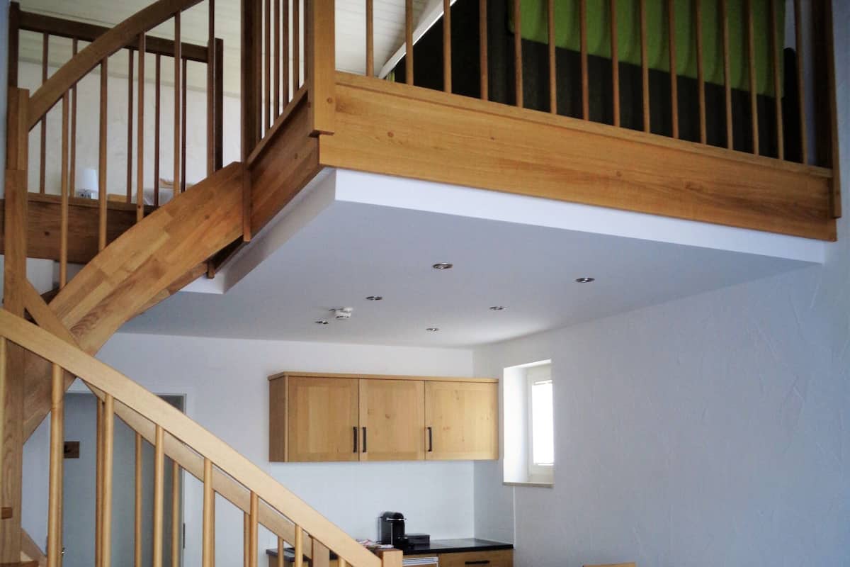 A multi-level wooden staircase connecting two floors, a dining area with a table and chairs, and a kitchen area with cabinets and a coffee maker.