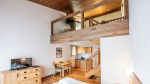 A bedroom with a wooden bed, a TV on a wooden dresser, and a staircase leading to a kitchen. -  Interest Vitalhotel (Oberstaufen)