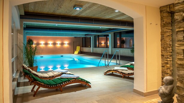 An indoor swimming pool with lounge chairs and a stone wall. -  Interest Vitalhotel (Oberstaufen)