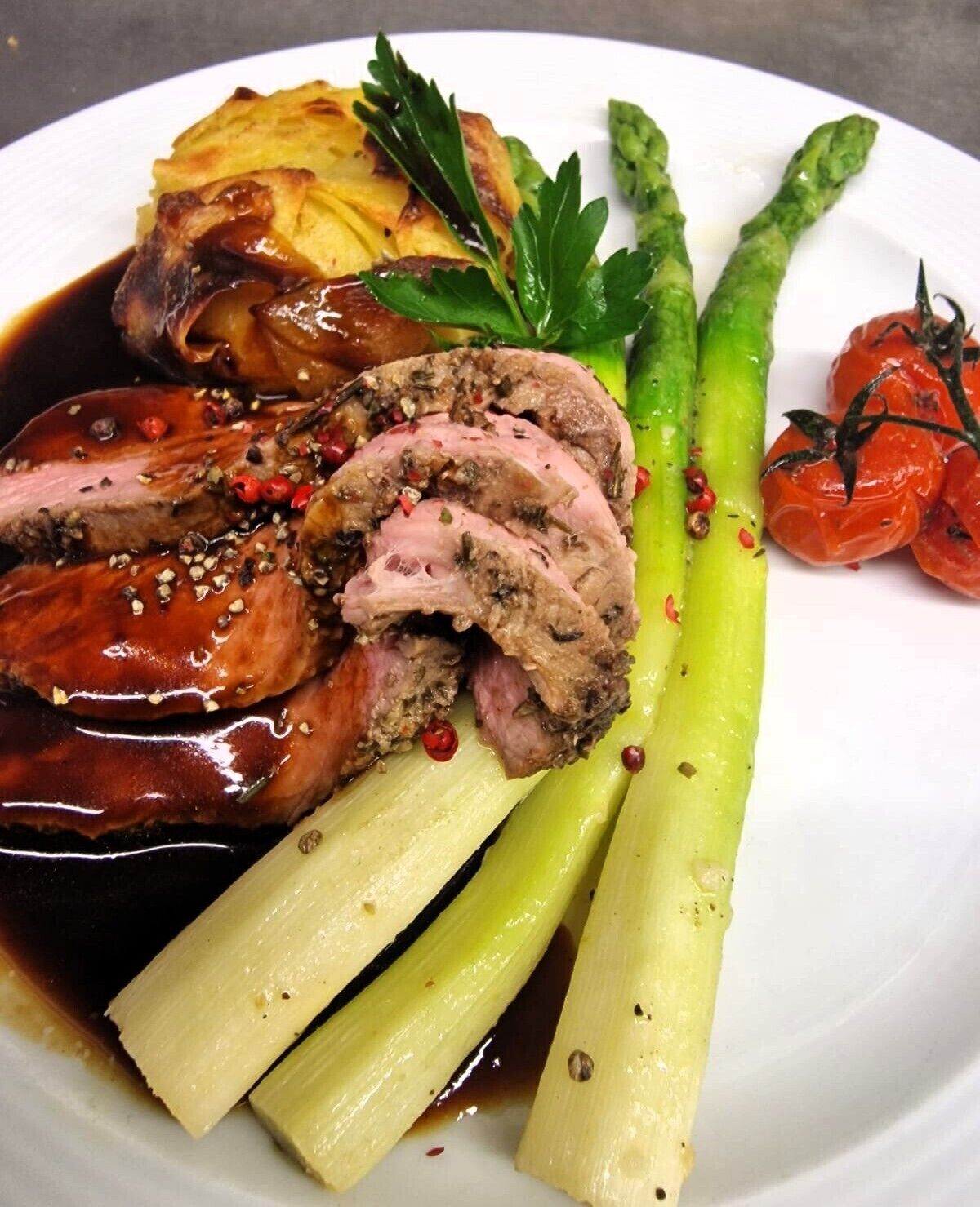 A plate with sliced meat, asparagus, and cherry tomatoes.