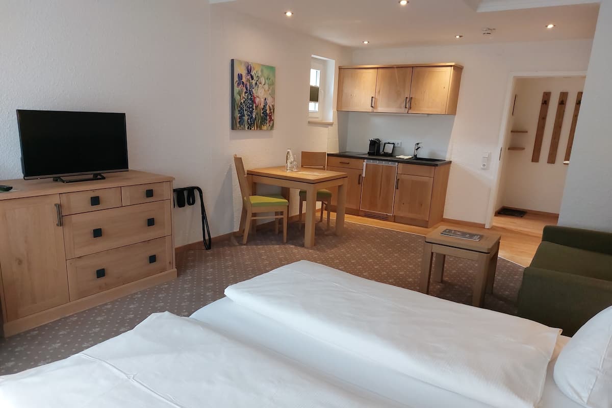 A hotel room with a bed, a desk, a chair, a television, a painting, and a kitchenette.