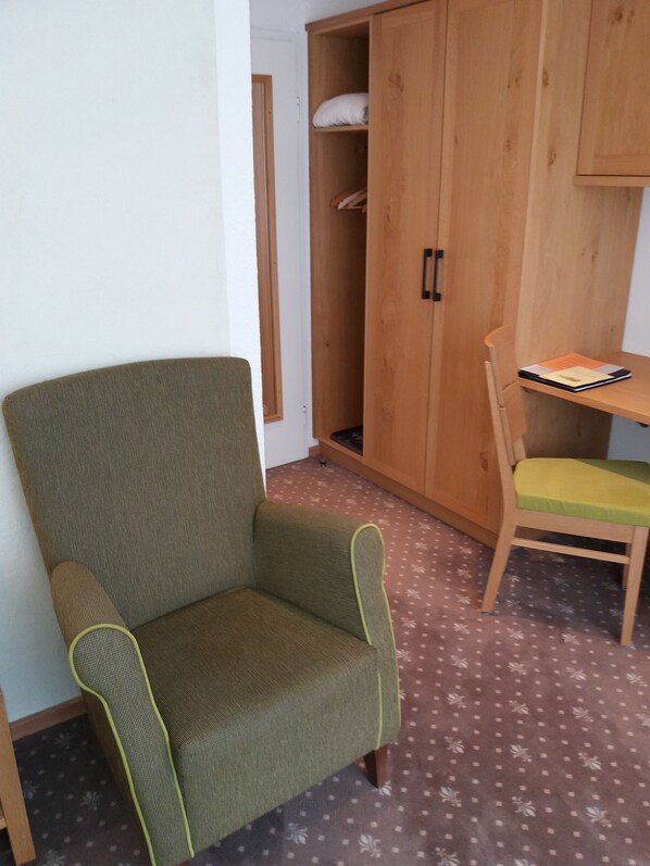 A room with a green armchair, a wooden cabinet, and a small wooden table with a chair. - Interest Vitalhotel (Oberstaufen)