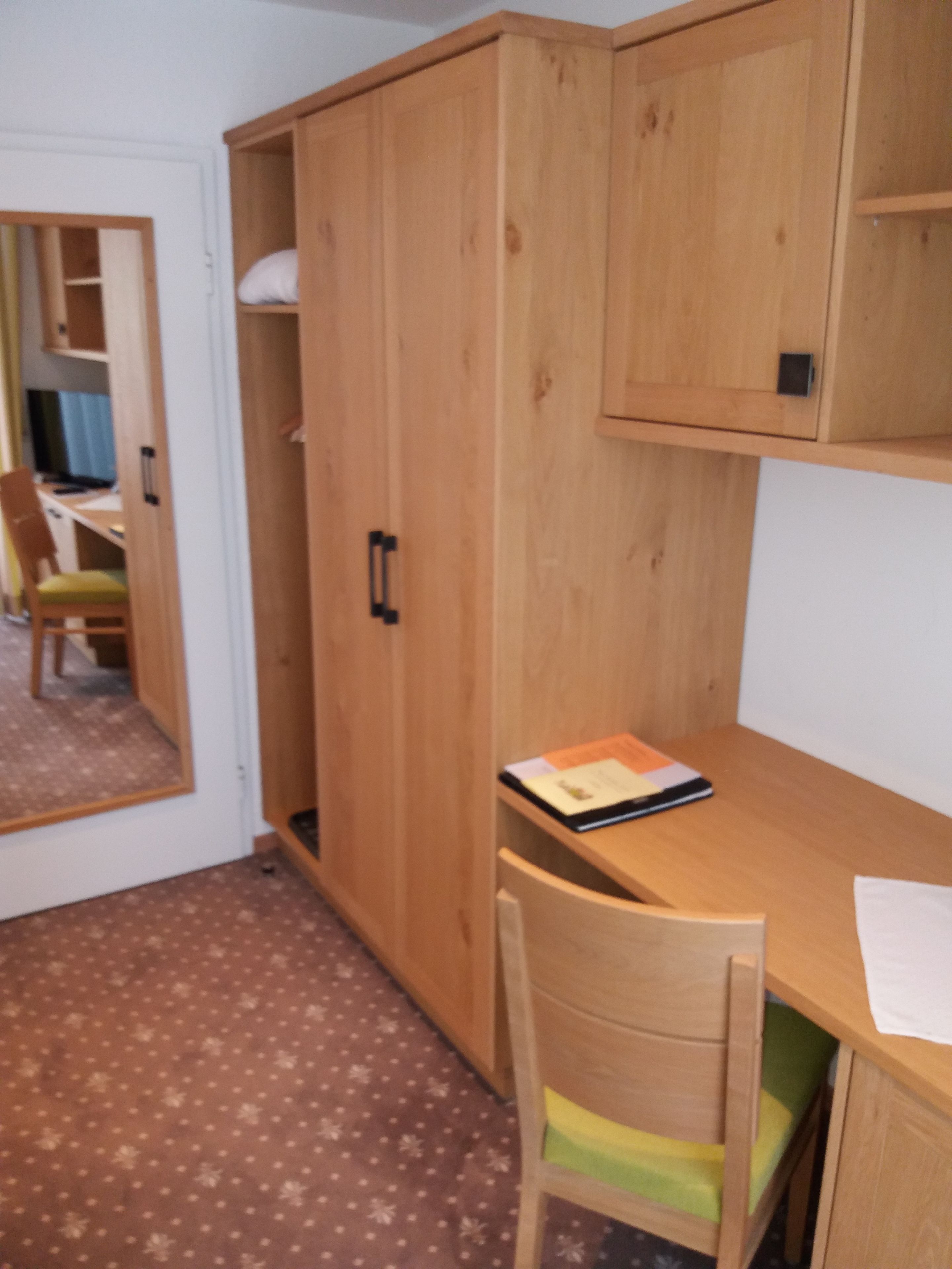 Una habitación con un escritorio de madera, una silla, un armario y un espejo.