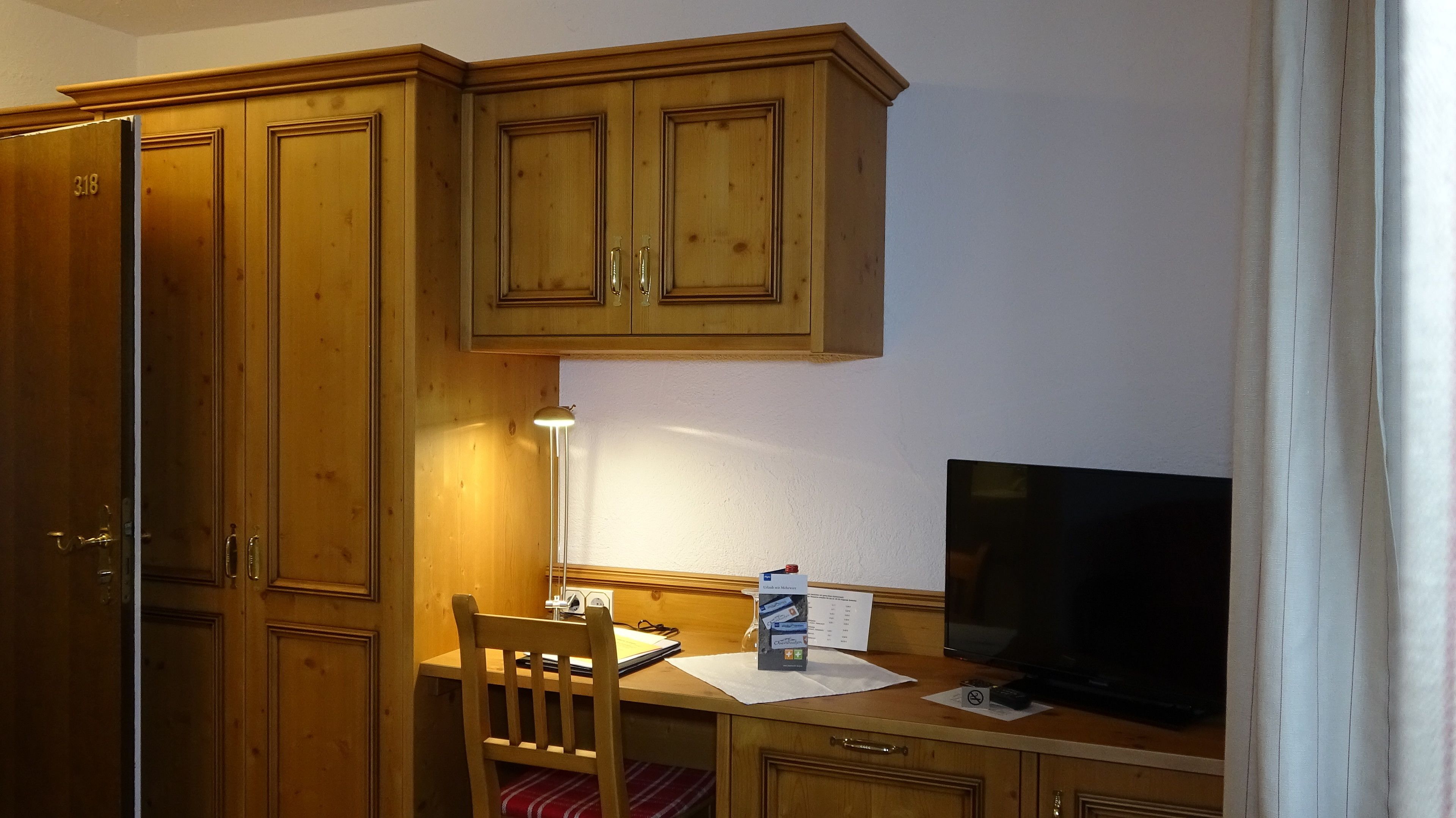 A wooden desk with a television, a chair, and a lamp.
