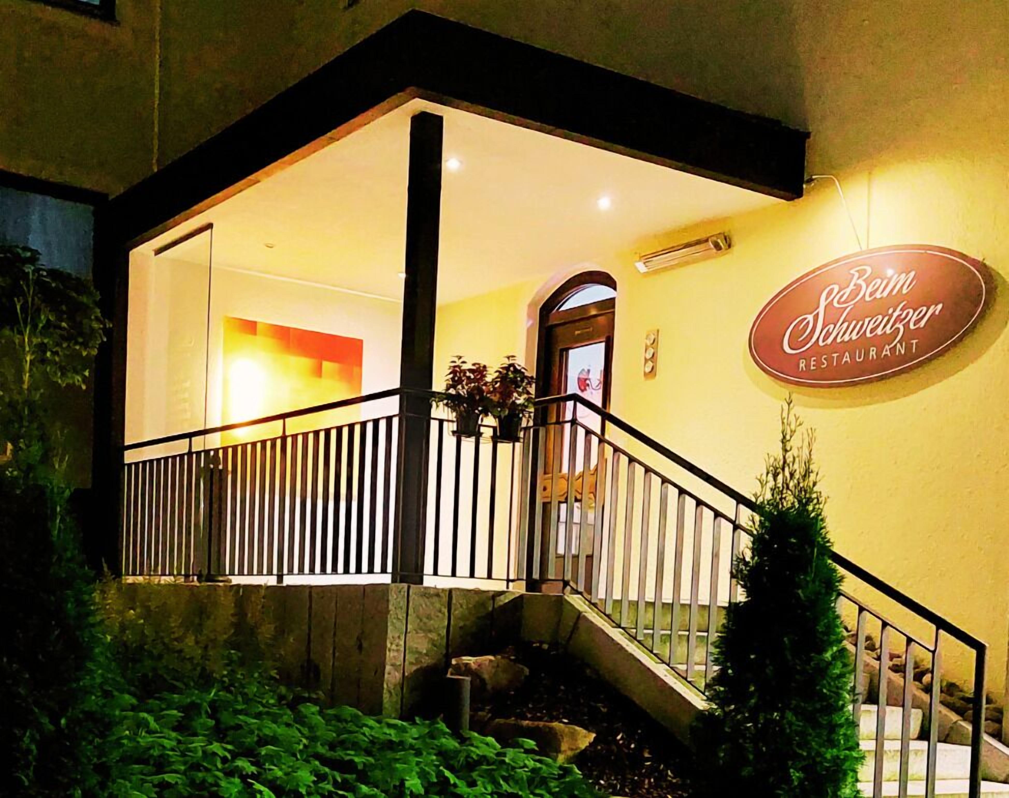 A restaurant entrance with a staircase, a railing, and a sign that reads "Beim Schweitzer Restaurant".