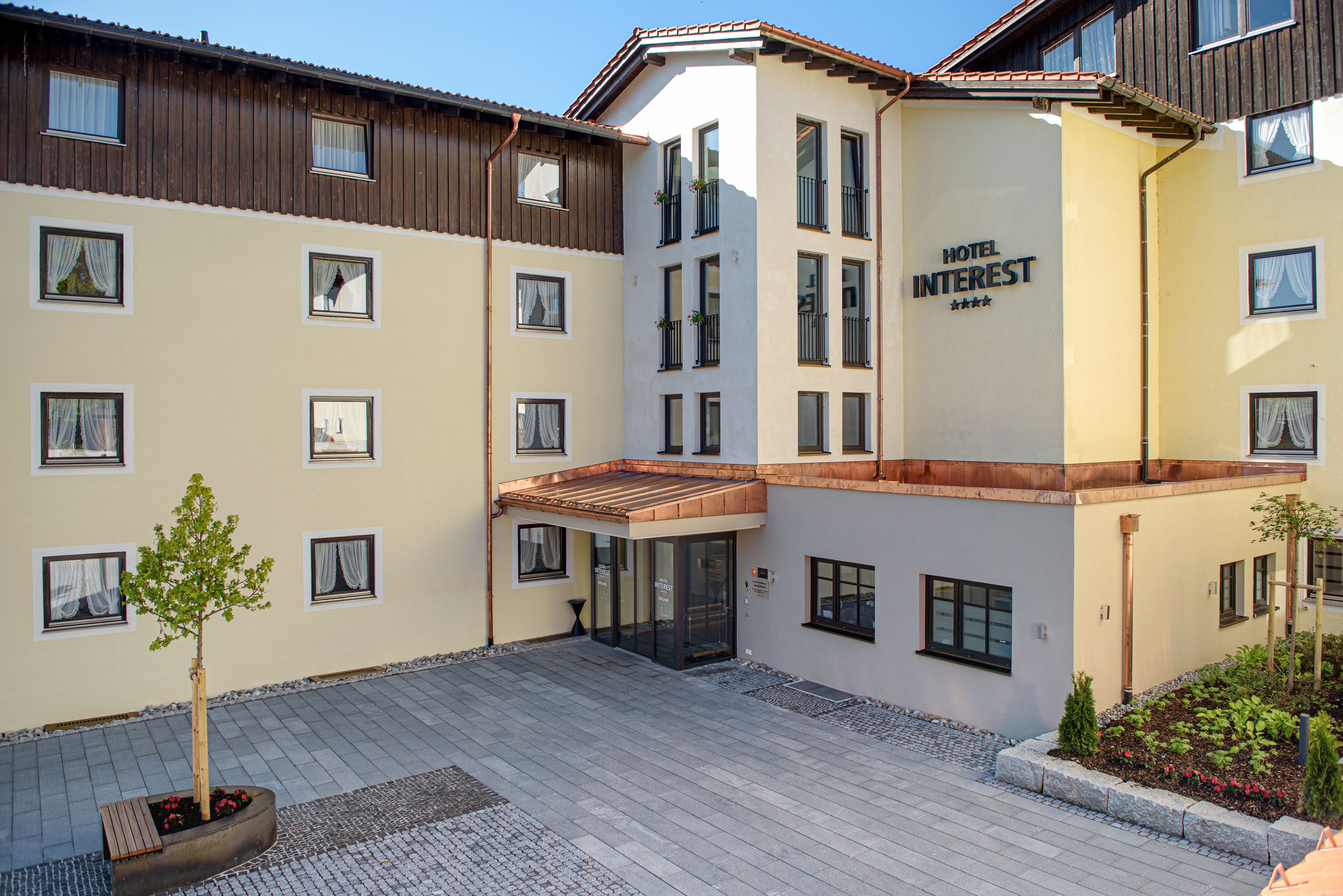 A hotel with a modern design, featuring a courtyard with a small tree and a seating area.