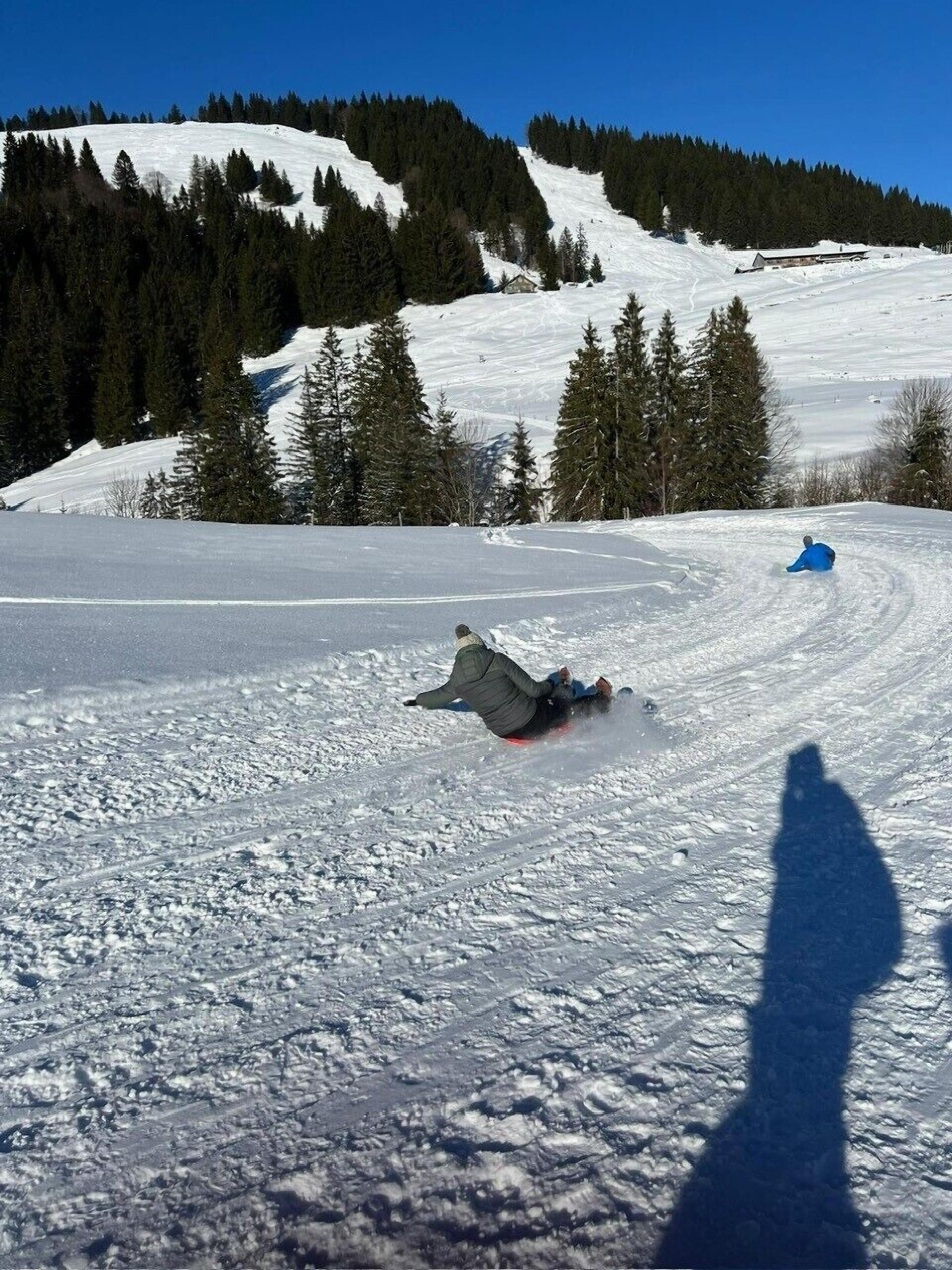 Schneebedeckte Landschaft mit einer Rodelbahn und dem Schatten einer Person.