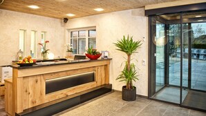 A reception desk with a wooden finish, a potted plant, and a fruit bowl. -  Interest Vitalhotel (Oberstaufen)