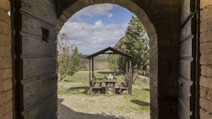 An arched stone doorway leading to a covered outdoor seating area with a table and benches. - Wine Resort Colsereno (Montalcino)