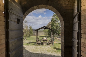 Un arco de piedra da acceso a un área cubierta con mesas y bancos.